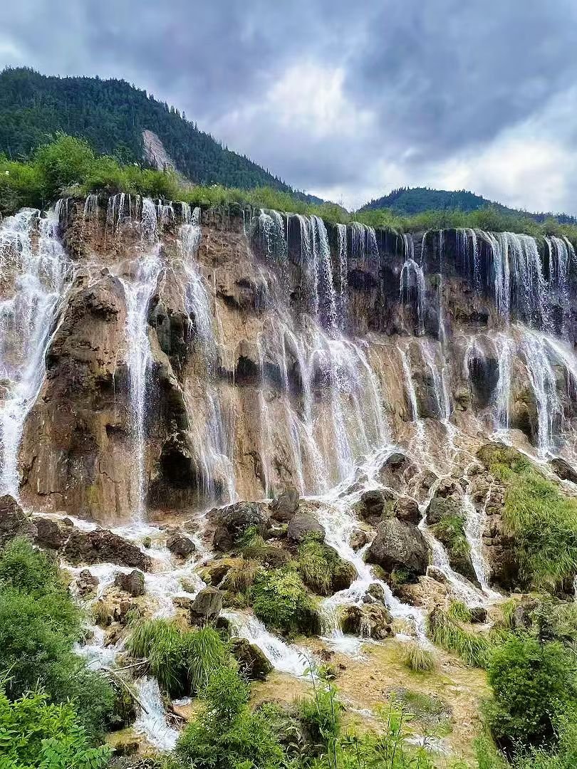 Traveler photographing a turquoise Jiuzhaigou lake with a smartphone